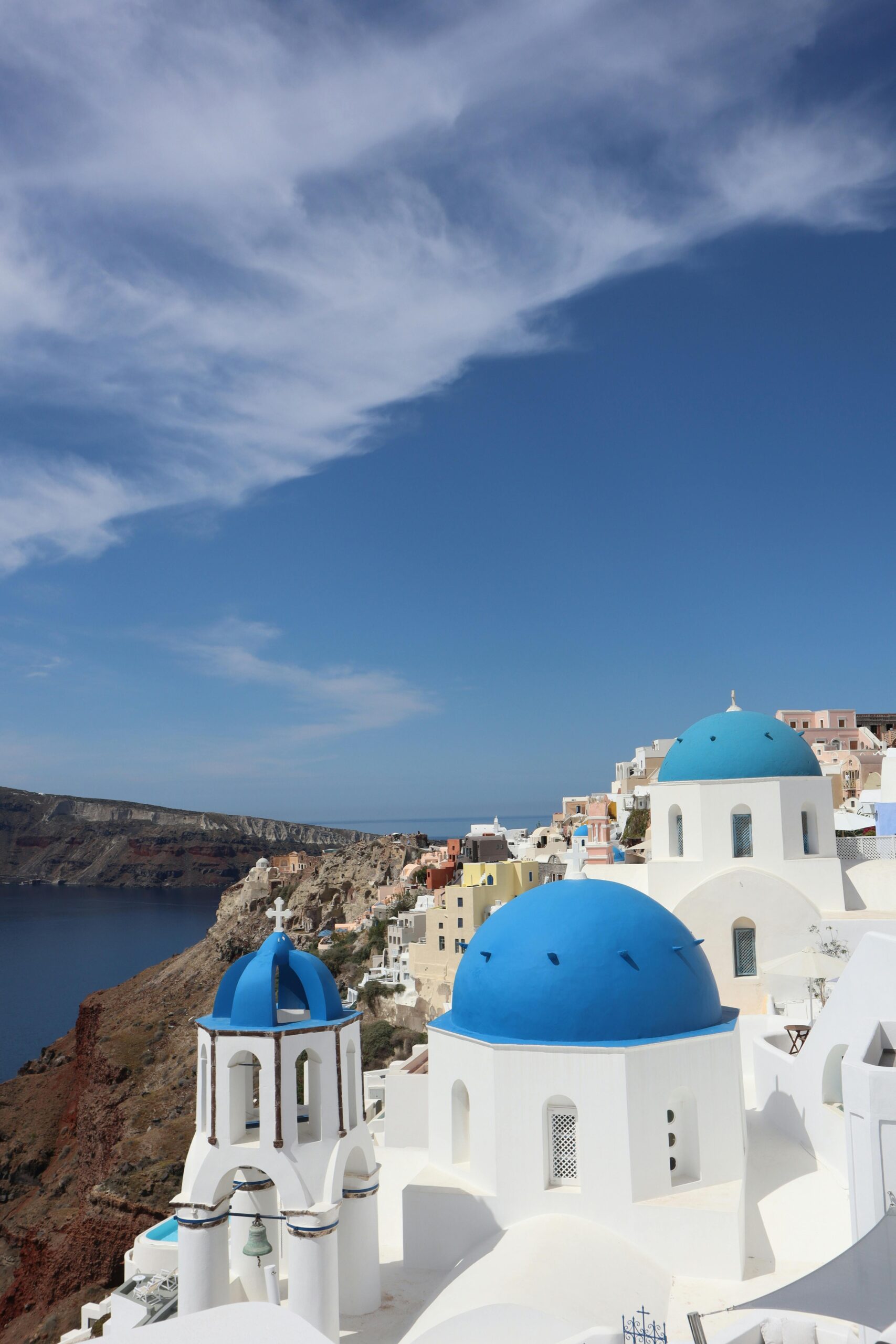 Iconic blue-domed churches in Fira, Santorini against a clear blue sky and the Aegean Sea.